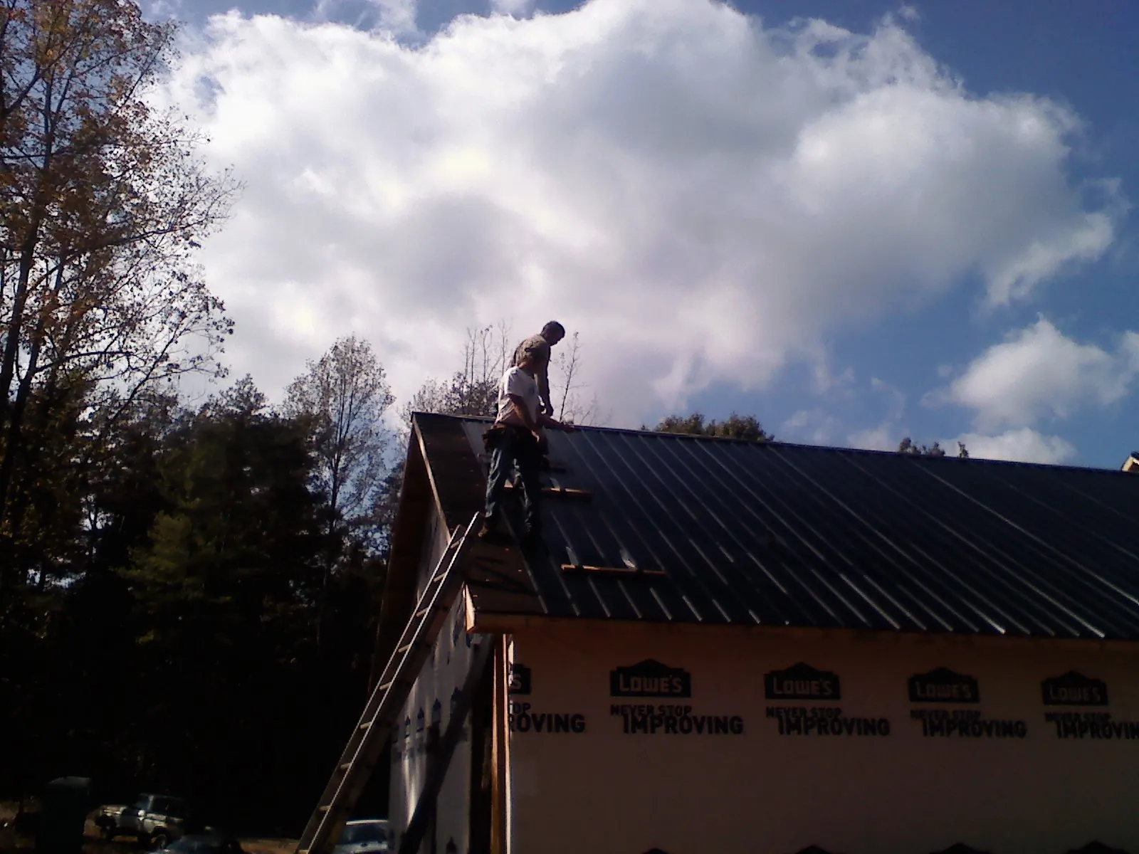Roofer fastening dark metal panels high against a cloudy sky, from a Roof Inspection job in Ash Fork